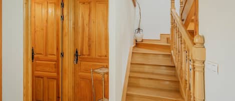 Una escalera de madera con barandilla y una puerta con un estante metálico.
