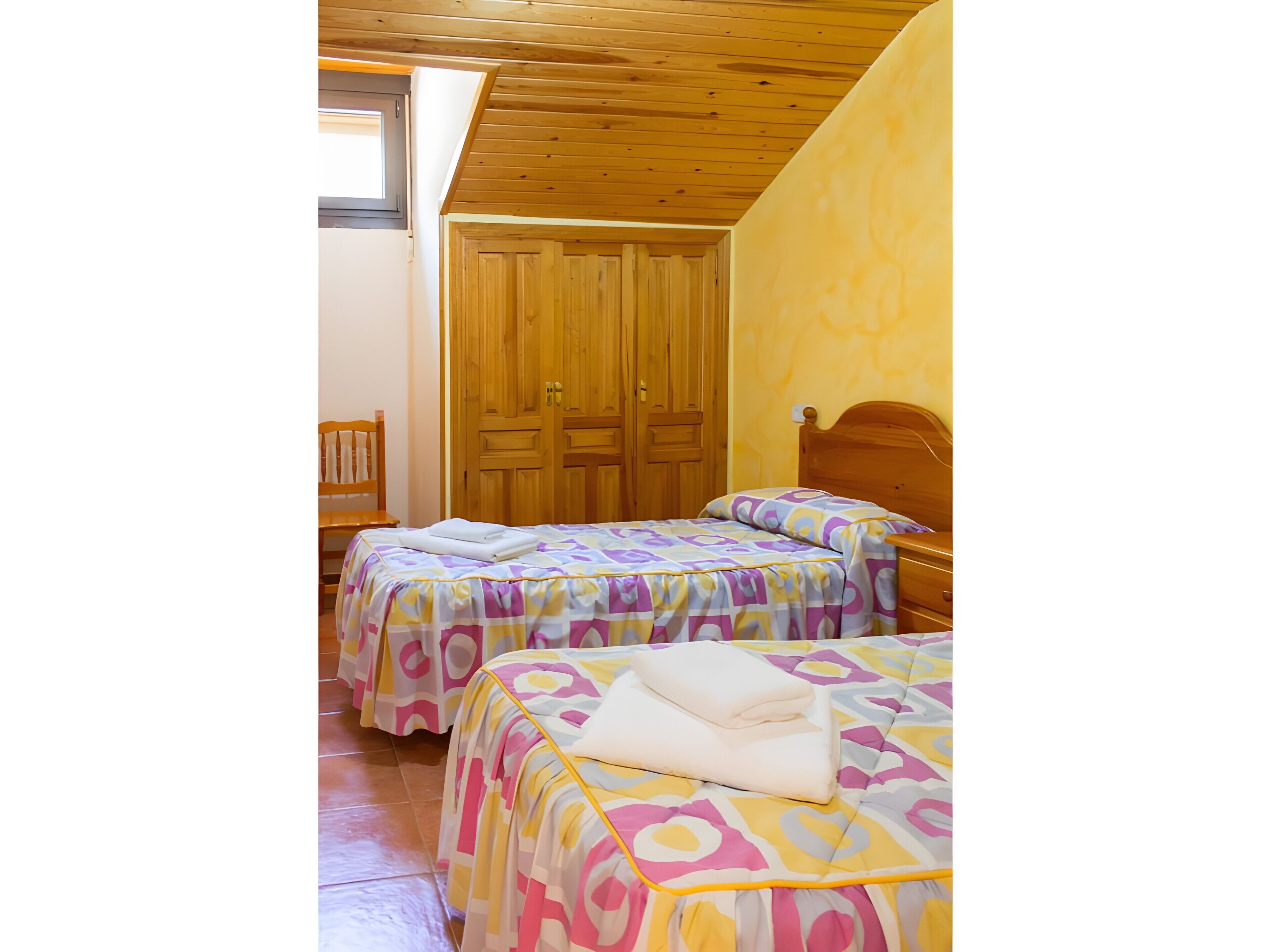 Ein Zimmer mit zwei Betten, Holzboden und einem Holzschrank.
