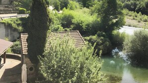 A riverside view with a mountain in the background, a building with a tiled roof, and lush greenery. - Apartment 'Yerga' with Wi-Fi (Tella)