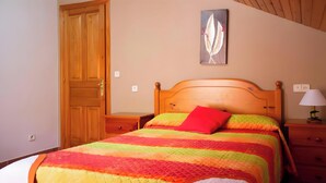 A bedroom with a wooden bed, a colorful quilt, a red pillow, a nightstand with a lamp, and a door. - Apartment 'Santa Justa' with Mountain View, Wi-Fi and Air Conditioning (Hospital)