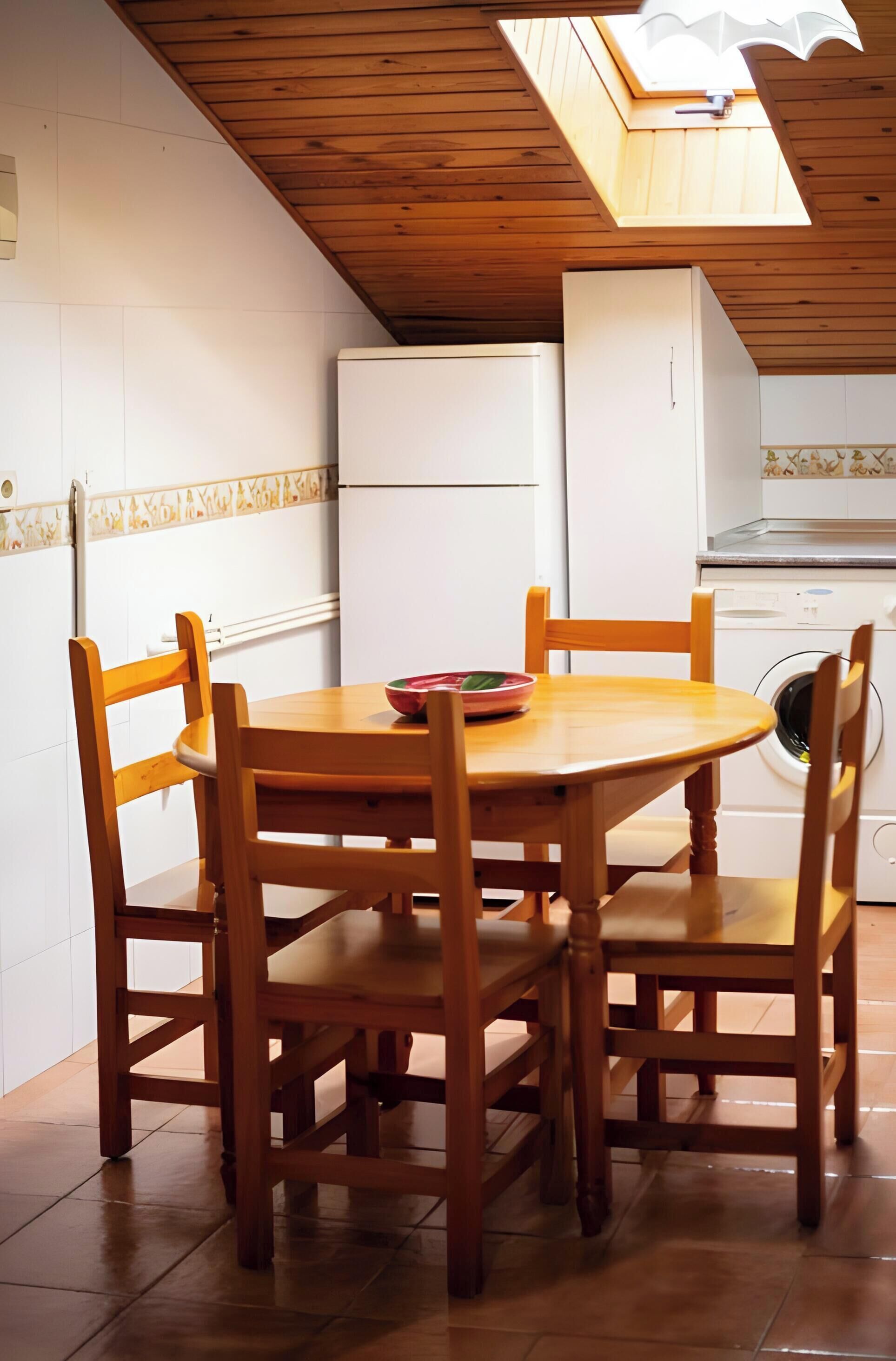 Una cocina con una mesa y sillas de madera, un refrigerador blanco y una lavadora.