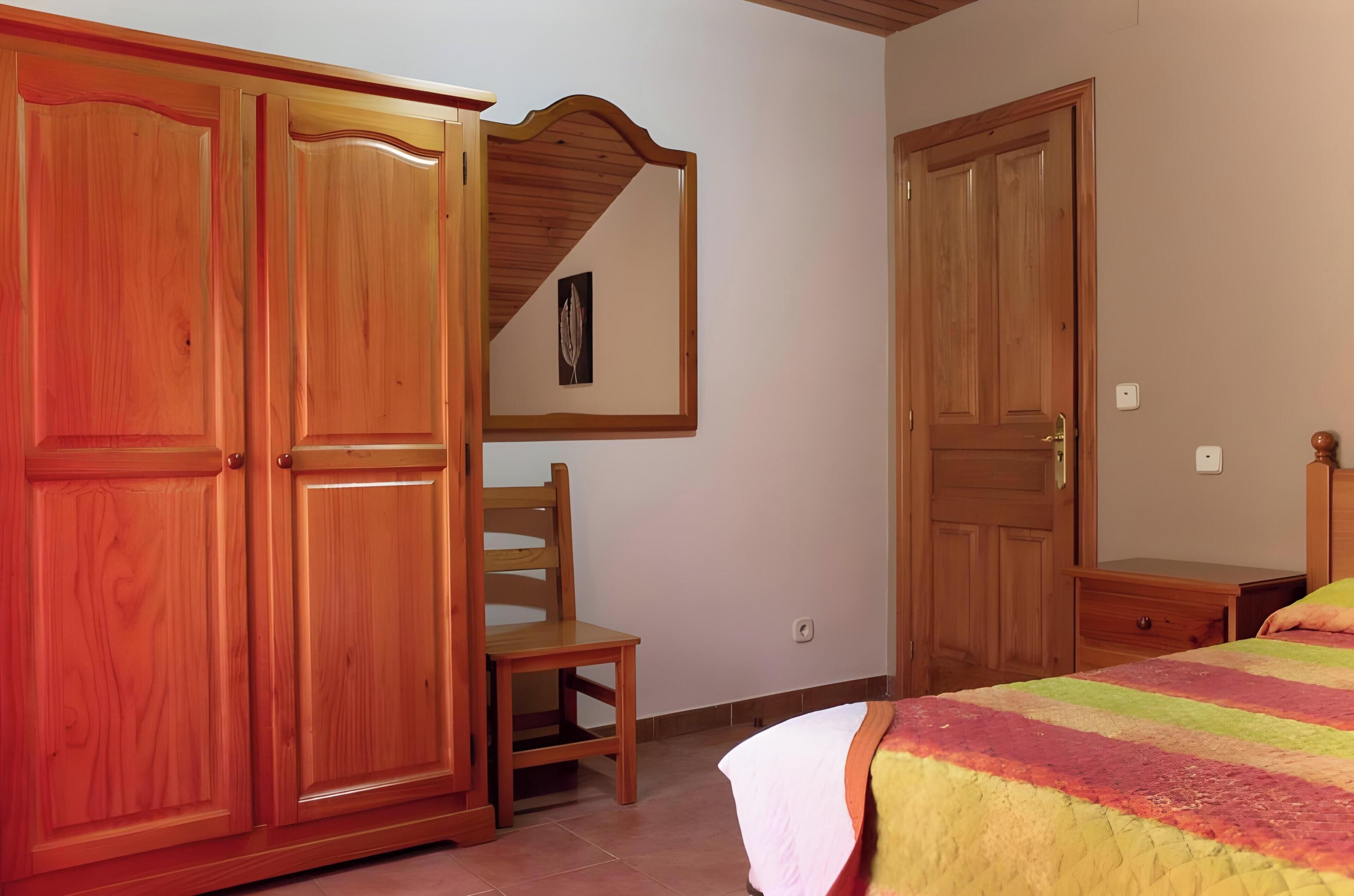 Un dormitorio con armarios de madera, una silla, una cama con manta a rayas y un espejo en la pared.