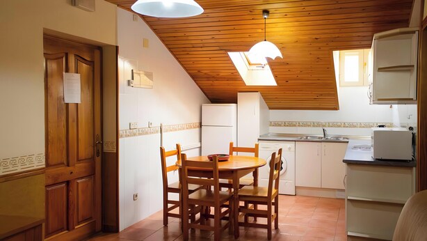 A kitchen with wooden cabinets, a dining table with chairs, a built-in oven, and a window above the sink. - Apartment 'Santa Justa' with Mountain View, Wi-Fi and Air Conditioning (Hospital)