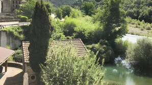 A riverside view with a mountain in the background, a building with a tiled roof, and lush greenery. - Apartment 'Santa Justa' with Mountain View, Wi-Fi and Air Conditioning (Hospital)