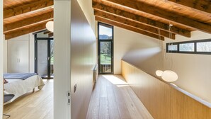 A modern loft bedroom with a sloped ceiling, wooden beams, a large window, and a view of the outdoors.
