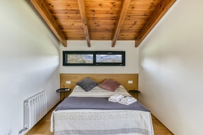 Una habitación estrecha con techo de madera, una cama con almohadas, un radiador y dos cuadros en la pared.