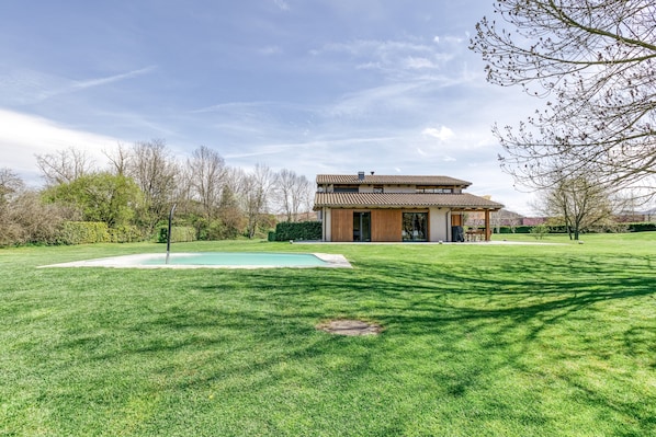 Una casa moderna con piscina, rodeada de césped cuidado y árboles.