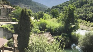 A riverside view with a mountain in the background, a building with a tiled roof, and lush greenery.