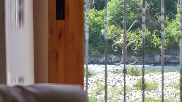 A room with a wooden door, a view of a river, and a balcony with metal railings.