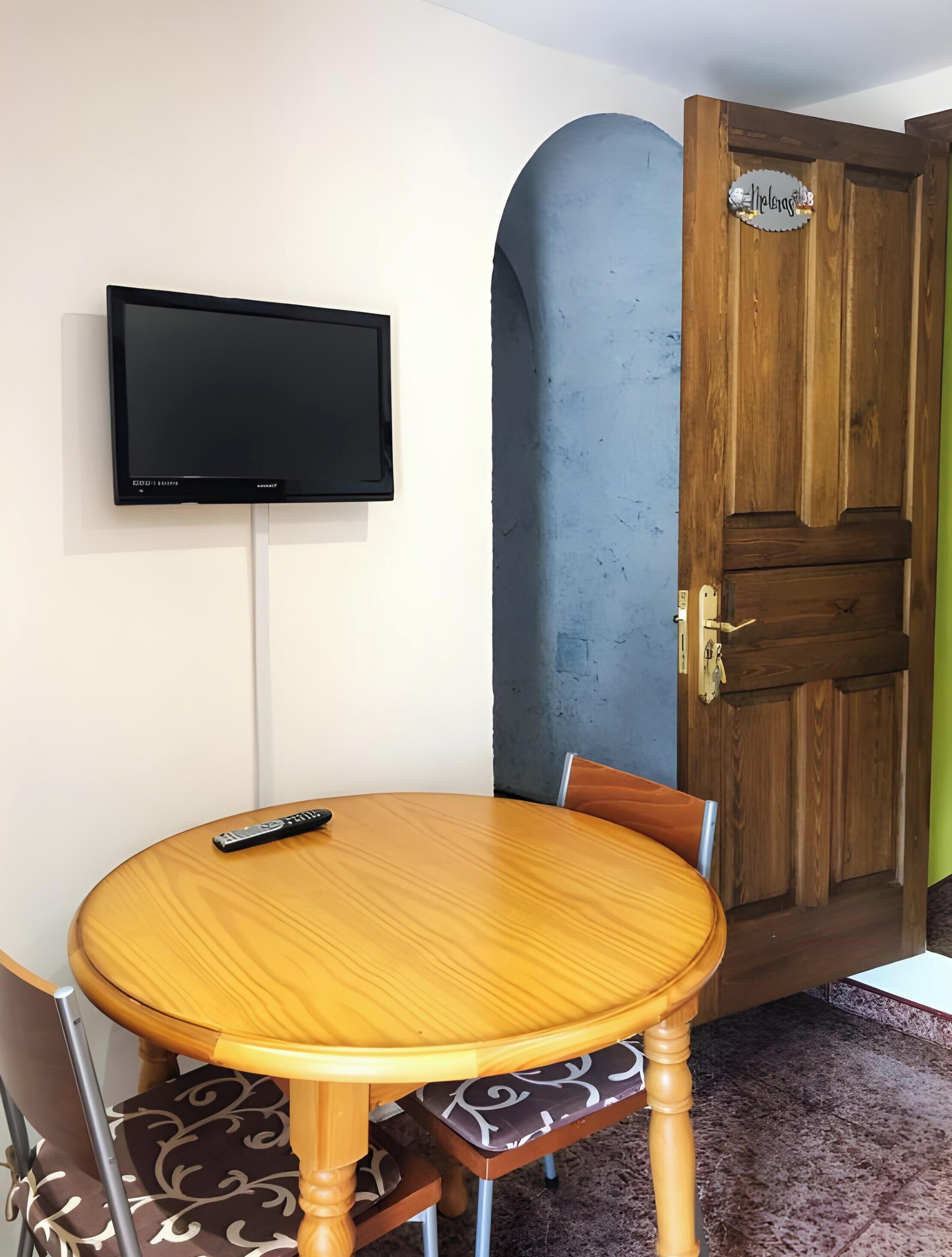 Une pièce avec une table ronde en bois, un téléviseur fixé au mur et une porte en bois avec une pancarte.