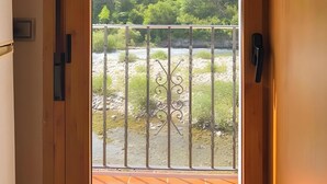 A wooden door with a view of a balcony overlooking a river and forested hills.