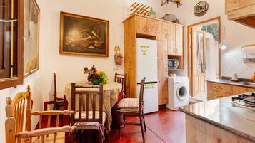 A kitchen with wooden cabinets, a dining table with chairs, a refrigerator, a washing machine, and a painting on the wall.