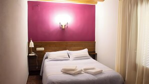 Una cama bien tendida con almohadas y toallas dobladas, una lámpara de noche y una lámpara de pared.