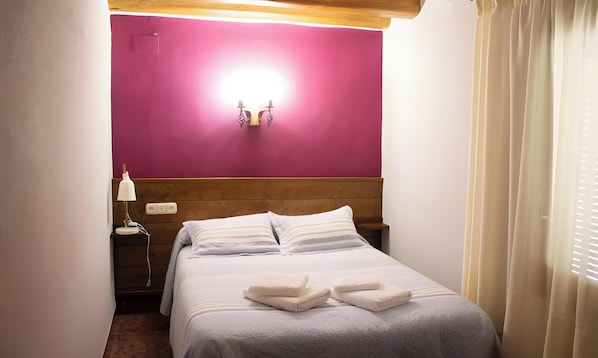 Un llit ben fet amb almoines i tovalloles netejades, una làmpada de nit i una làmpada de paret.