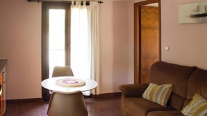 Un salón con un sofá marrón, una mesa redonda con un mantel individual y una ventana con cortinas.