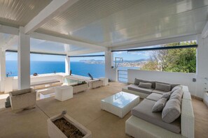 A modern outdoor living space with a view of the sea, a pool, and a seating area.