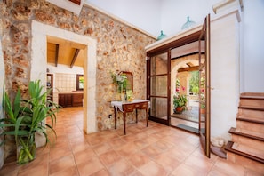 A stone-walled interior with a wooden table, a potted plant, and a view of a garden through a glass door. - Country House 'Es Matul-los Ref 134' with Mountain Views, Private Pool and Wi-Fi (Sant Llorenç Del Cardassar)