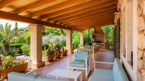 A covered patio area with outdoor seating, a bar, and a view of lush greenery.