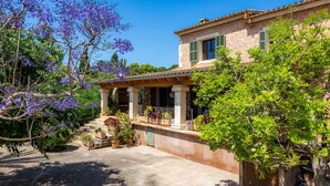 A traditional Mediterranean-style building with a stone facade, green shutters, and a covered porch with potted plants.