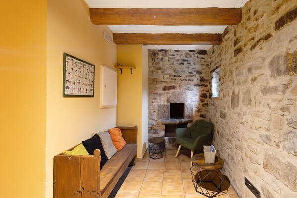 A cozy room with a stone wall, a wooden bench, a green chair, and a small table with a basket. - Country House 'La Serra' with Mountain View, Private Pool and Wi-Fi (Vilada)