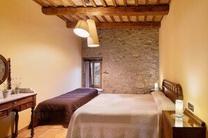 Une chambre avec un mur en pierre, des poutres en bois, un lit, une table de chevet et une commode.