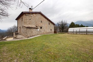 Un bâtiment en pierre avec un toit en pente, un petit escalier menant à l’entrée et une pelouse devant.