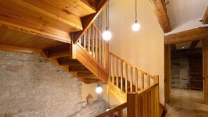Un escalier en bois, avec un mur en pierre, une rampe en bois et des luminaires suspendus.