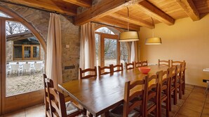 Un espace repas avec une table et des chaises en bois, des murs en pierre et de grandes fenêtres.