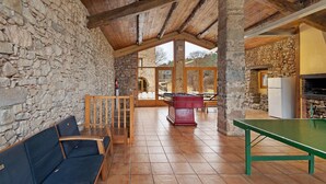 Une pièce aux murs de pierre, avec des poutres en bois, une table de ping-pong, un canapé et, au fond, une autre table de ping-pong.