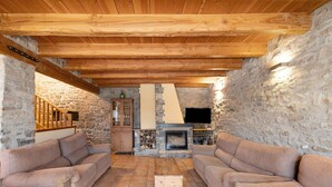 Un salon chaleureux avec des murs en pierre, des poutres en bois, une cheminée et deux canapés.