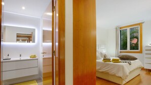 Un dormitorio moderno con cama, mesita de noche y ventana con vista a palmeras.