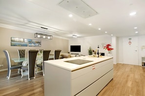 Una cocina moderna con una isla central, comedor con sillas, televisor de pantalla plana y obras de arte en la pared.