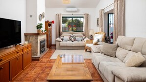 A living room with a TV, sofa, coffee table, fireplace, and a view through a window. - Holiday Home 'Palmera' with Mountain View, Private Pool and Wi-Fi (Málaga)