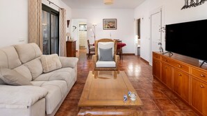 A living room with a sofa, a wooden coffee table, a television, and a dining area with chairs. - Holiday Home 'Palmera' with Mountain View, Private Pool and Wi-Fi (Málaga)