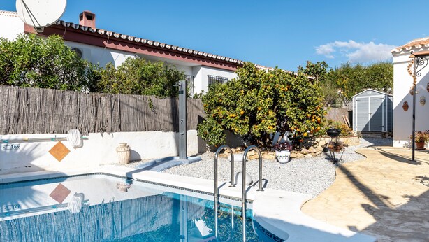 A swimming pool with a wooden fence, a small garden with trees and a barbecue, and a shed in the background. - Holiday Home 'Palmera' with Mountain View, Private Pool and Wi-Fi (Málaga)