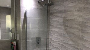 Un baño moderno con ducha envuelta en vidrio, una bañera blanca y un lavabo con artículos de aseo.