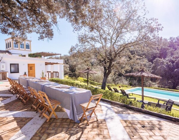 An outdoor dining area with a checkered tablecloth, wooden chairs, and a poolside view.