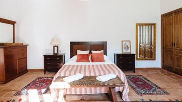 Un dormitorio con una cama, dos mesitas de noche, un aparador de madera, un espejo y alfombras estampadas.