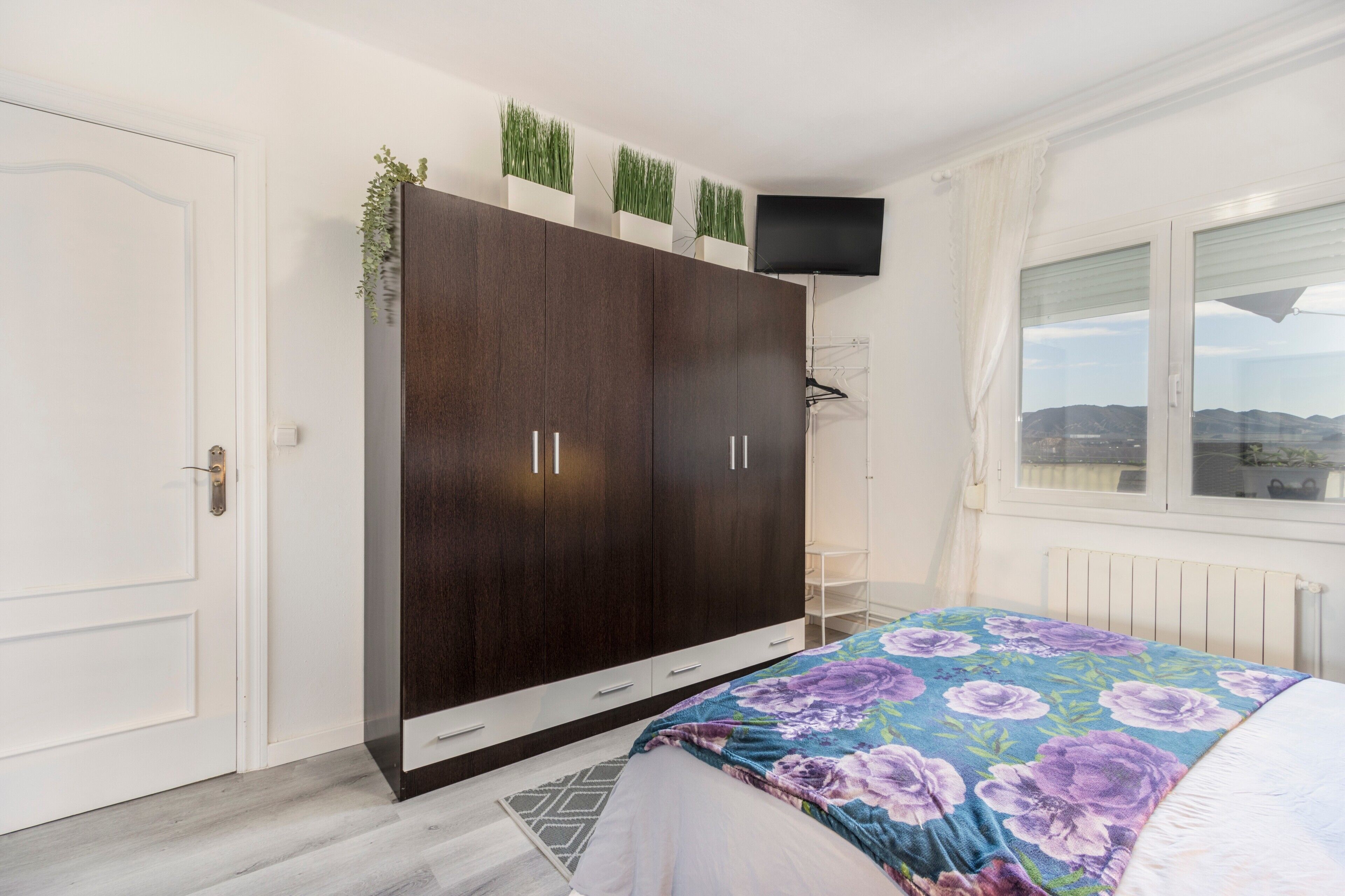 Een slaapkamer met een grote garderobe, een bed met een bloemenbedekking, en een raam met uitzicht.