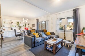 A modern living room with a grey sofa, a wooden coffee table, and a dining area with a table and chairs.