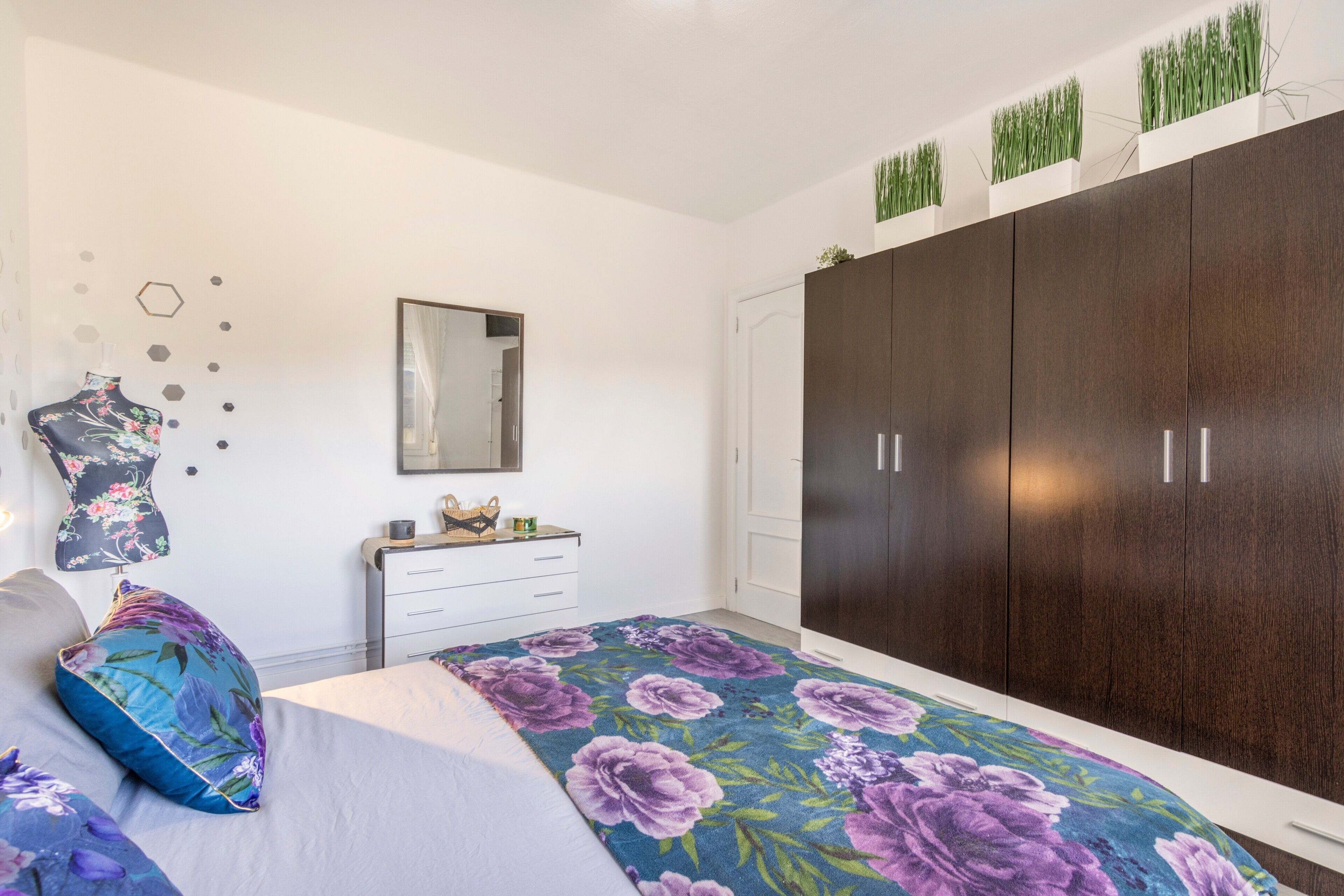 Un dormitorio con cama, cómoda, armario, espejo y adornos en la pared.