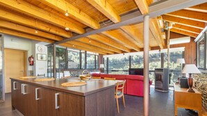 A spacious kitchen with a central island, a red sofa, a fireplace, and large windows offering a view of the outdoors.