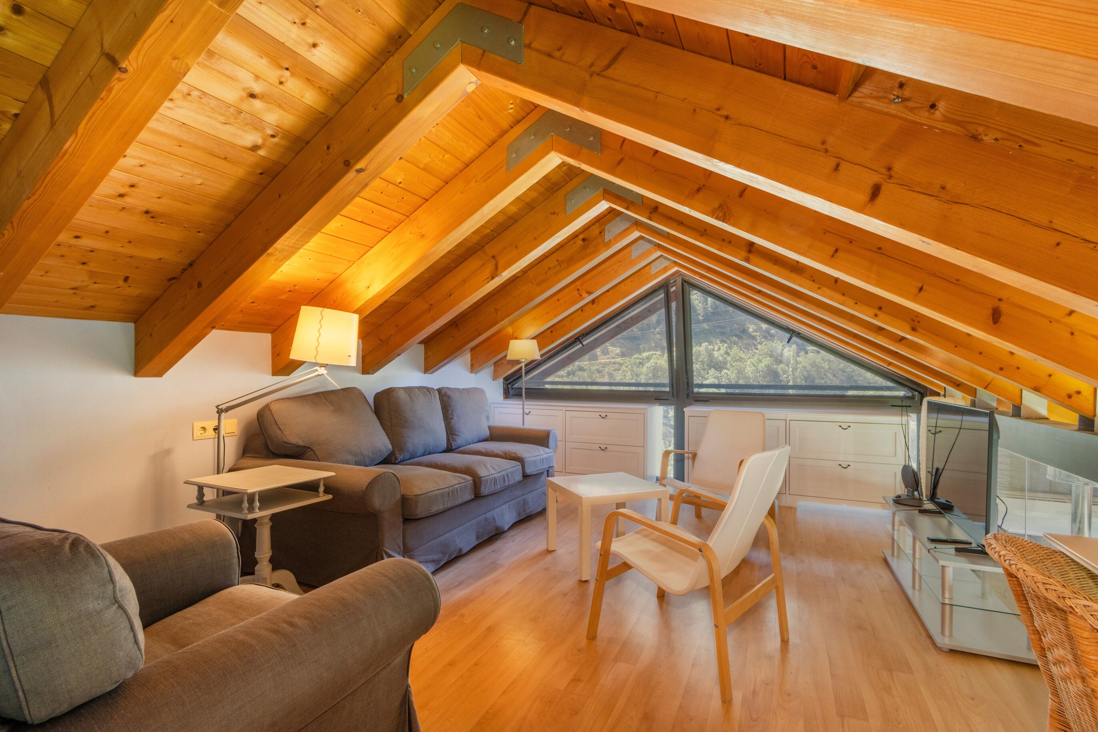 An attic bedroom with a sloped ceiling, a sofa, a chair, a desk, and a window.