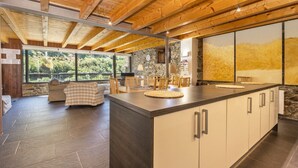A modern kitchen with a large island, stone walls, and a view of greenery.