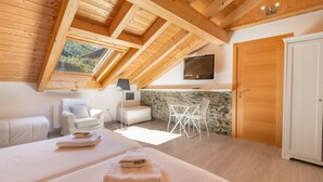 A bedroom with a sloped ceiling, a TV mounted on the wall, a stone wall, and a wooden door.