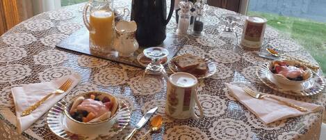 Une table de petit-déjeuner dressée avec différents plats, notamment un saladier de fruits, une cafetière et un pichet de jus.