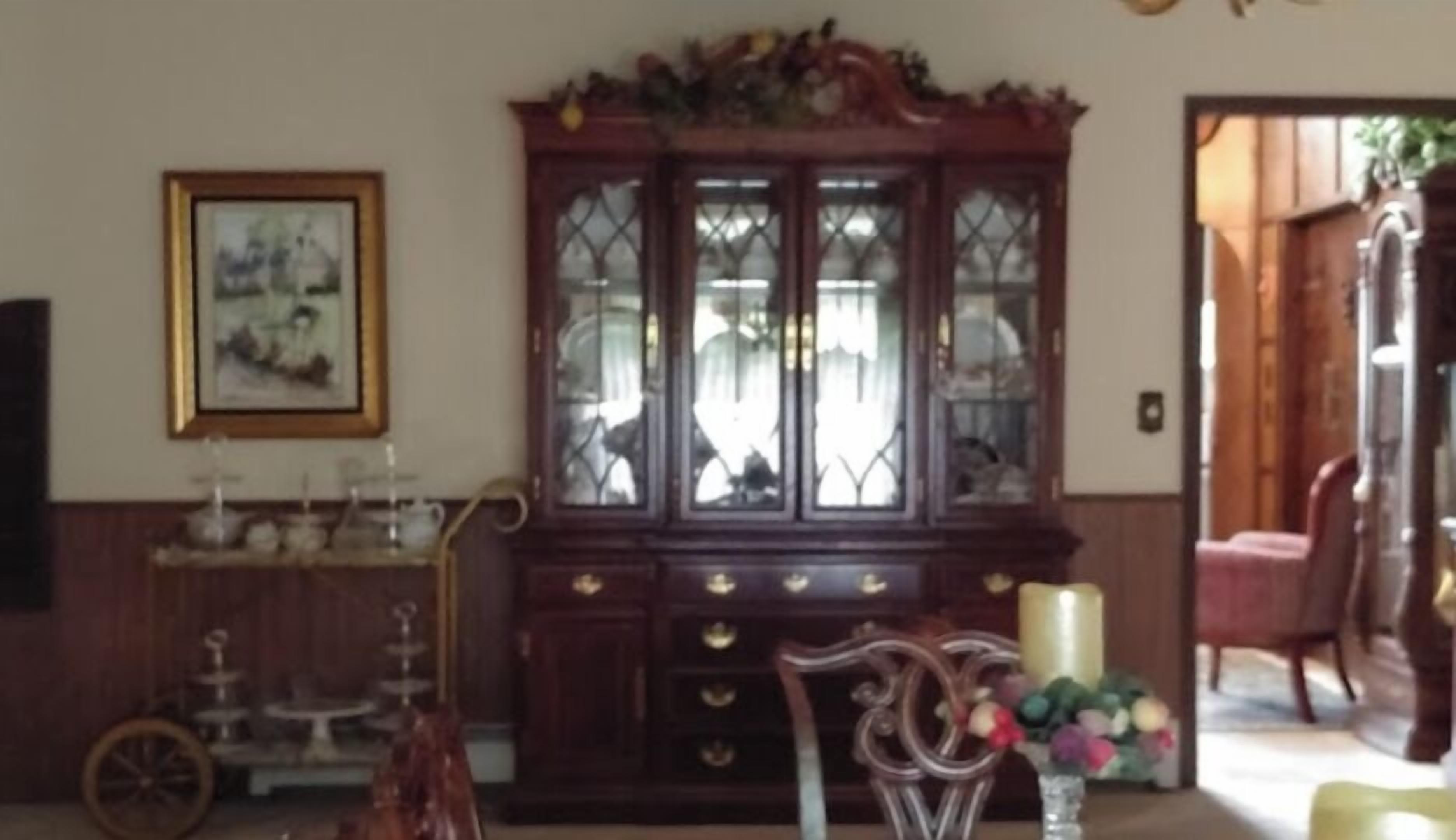 A traditional dining room with a wooden cabinet, a vintage chair, and a vase with flowers.