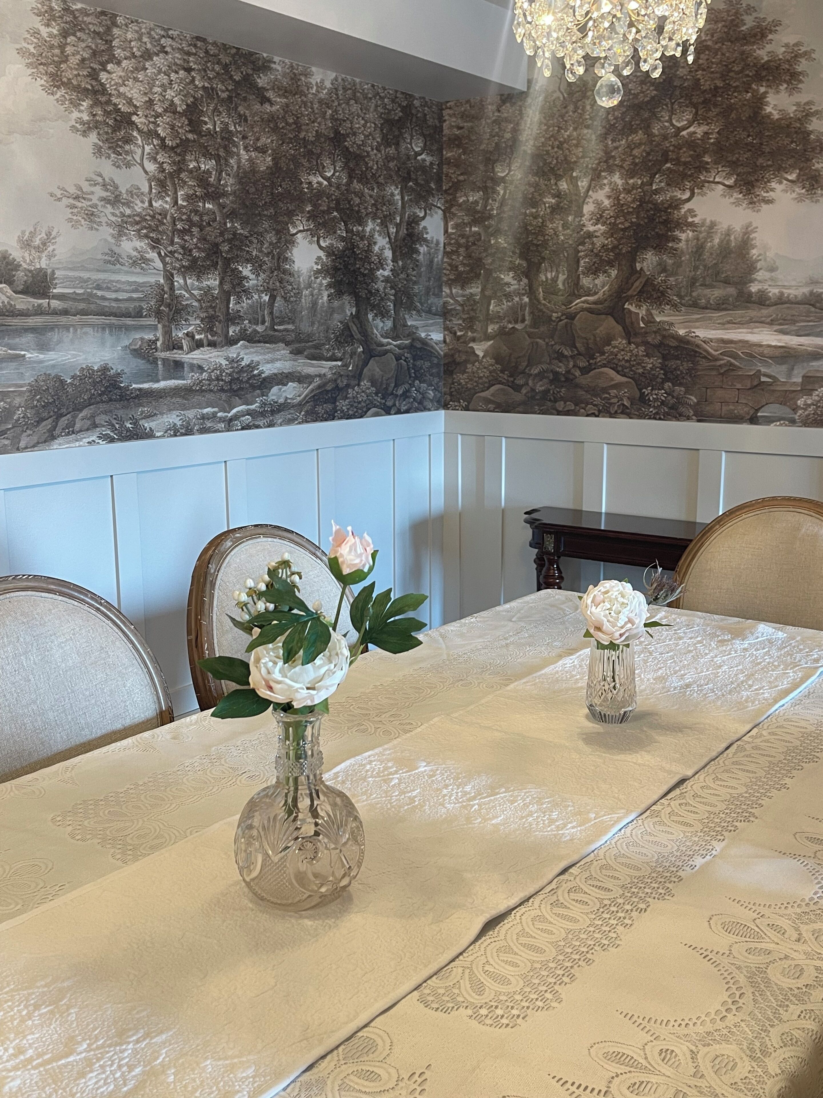 A dining area with a table set for two, featuring a floral centerpiece and a detailed mural on the wall.