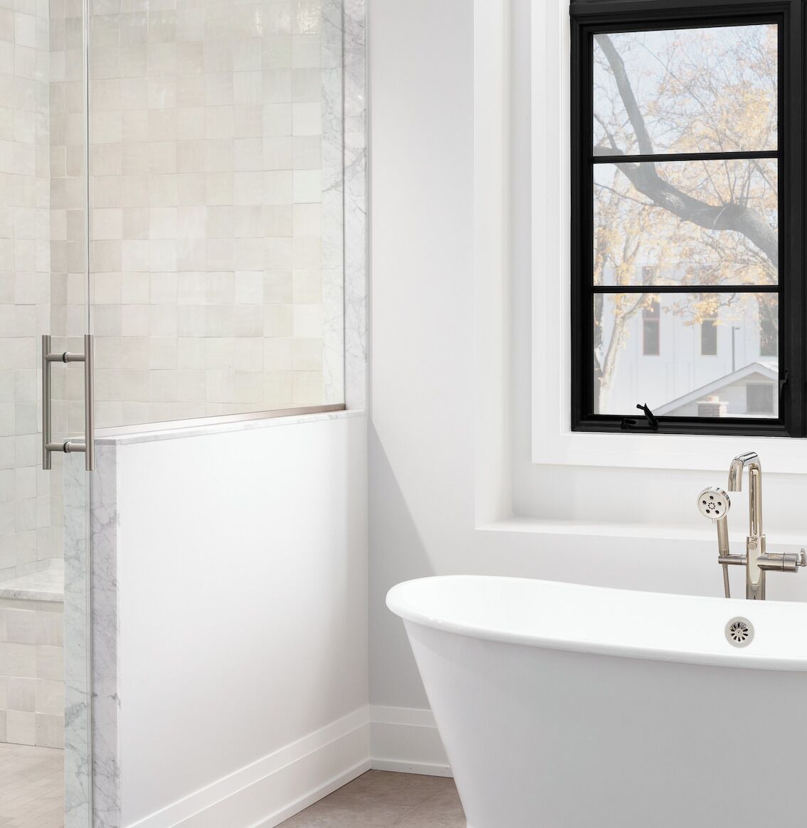 Un baño con cabina de ducha de vidrio, una bañera independiente y una ventana con vistas a árboles.