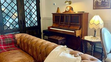 Uma sala de estar com um sofá de couro marrom, um piano de madeira e um abajur de renda.